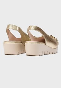 Sandalias de tirantes de imitación cuero dorado con una plataforma gruesa beige, que presentan un upper texturizado y un diseño de punta cerrada.
