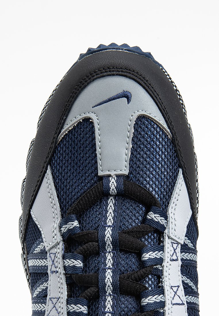 Nike-Schuh mit einem strukturierten navyblauen Mesh-Obermaterial, grauen Lederakzenten und einer schwarzen Gummi-Zehenkappe. Verfügt über dicke Schnürsenkel und ein auffälliges Logo.