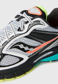 Close-up of a white, black, and neon green running shoe with detailed mesh, striped laces, and orange accent on the side.