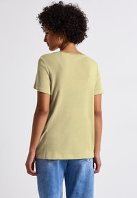 Kortärmad, ljusgrön topp i ett mjukt, strukturerat tyg med rund halsringning, i kombination med blå denimjeans.