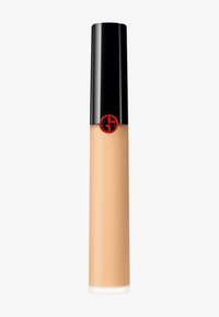Flytende foundation i en klar tube med svart hette. Inneholder en fremtredende rød, sirkulær logo. Produktet har en varm beige nyanse.