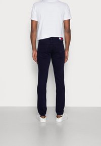 Vaqueros azul oscuro con un diseño ajustado y detalles de costura mínimos, combinados con una camiseta blanca de corte corto y zapatillas blancas.