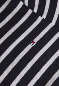 Gestreifter Stoff mit abwechselnd navyblauen und weißen Linien, vervollständigt mit einem kleinen, gestickten Logo in Rot, Weiß und Blau.