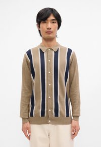 Brun och marinrandig cardigan med krage, framknappar och långa ärmar. Tillverkad av mjukt material med kontrasterande vita linjer.