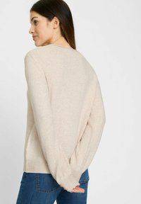 Hellbeiger Pullover mit weicher Textur, rundem Ausschnitt und langen Ärmeln. Verfügt über gerippte Bündchen und Saum, getragen mit blauen Jeans.