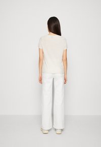 Camiseta de color beige claro con mangas cortas, combinada con jeans anchos blancos. La tela parece suave y con una ligera textura.