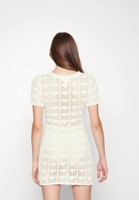 Vestito a maniche corte in crochet verde chiaro; presenta motivi geometrici e una silhouette aderente; scollatura e orlo smerlati.