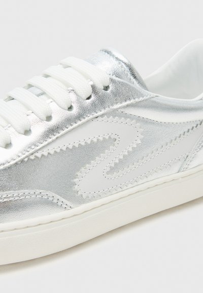 Silverfärgad läder sneakers med vita snören, med en texturerad yta och en vågig vit design längs sidan. Platt sula med minimal mönstring.
