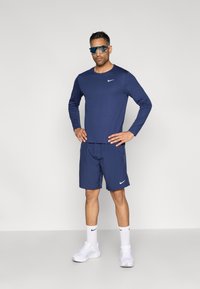 Marineblå Nike langermet topp og shorts; syntetisk stoff, rund hals, hvit logo, solbriller, hvite treningssko, teksturerte sokker.