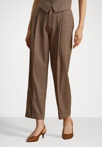 Braune, gemusterte Hose mit lockerer Passform, mit Falten an der Vorderseite und umgeschlagenen Säumen. Kombiniert mit braunen Slingback-Absätzen.