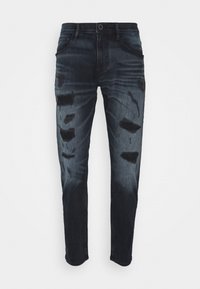 Tmavě modré džínové kalhoty s poškozením, obsahující několik roztržených částí a slim fit střih. Standardní pětikapsový styl.