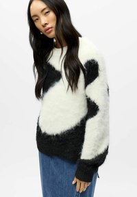 Kosete genser laget av mykt svart-hvitt strikket stoff med store abstrakte flekker. Lange ermer med ribbestrikkede mansjetter, kombinert med et denimskjørt.