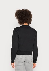 Sudadera negra de manga larga y cuello redondo, con un corte holgado y puños de canalé. Textura de tela suave, sin patrones visibles.