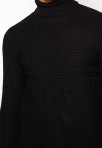 Pull noir à col roulé en tissu tricoté texturé avec des côtes verticales et une coupe décontractée. Caractérisé par un col montant et des manches longues.