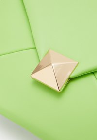 Vihreä keinonahkainen laukku, jossa on pyramidimuotoinen kultasulkija, sileä pinta ja taiteltu muotoilu.