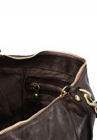 Interno di una borsa in pelle marrone con una cerniera dorata, dotato di una tasca con cerniera e scomparti aggiuntivi per l'organizzazione. Texture liscia.
