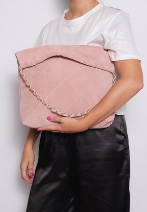 Borsa in suede rosa trapuntata con patta a ribalta e tracolla in oro, tenuta sotto il braccio. Texture liscia e dettaglio a motivo romboidale.