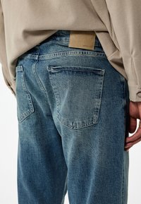 Vaqueros de mezclilla azul claro con un ajuste relajado, que cuentan con dos bolsillos traseros y una etiqueta de cuero marrón cerca de la cinturilla. Tejido texturizado.