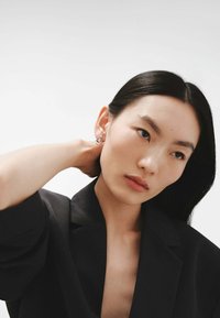 Pendientes de plata con un diseño geométrico, llevados por una persona en un blazer negro, que presentan texturas suaves y un acabado brillante.