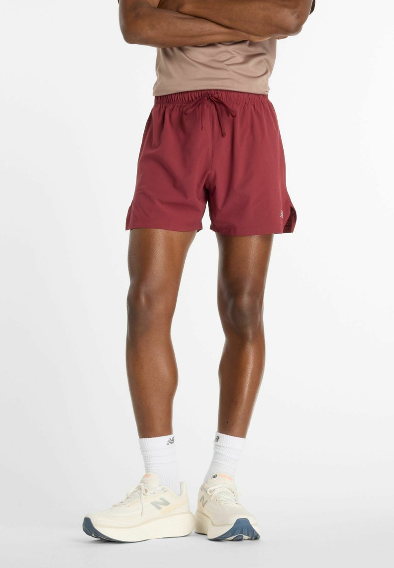 Pantaloncini color bordeaux con elastico in vita e coulisse, caratterizzati da spacchi laterali. Abbinati a scarpe da ginnastica chiare e calzini bianchi.