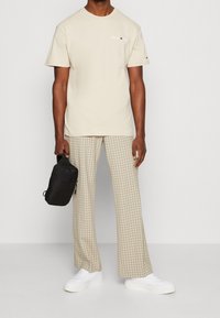 Beige cotton t-shirt with logo, paired with light plaid wide-leg trousers in cream and beige. White sneakers and a black bag.