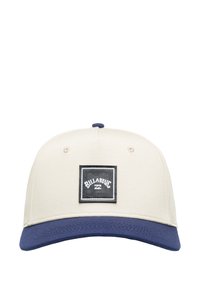 Beige pet met een marineblauwe rand, voorzien van een zwart vierkant patch met witte tekst en een gewaxte stof. Zes ventilatiegaten op de kroon.