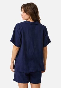 Ensemble de loungewear en coton respirant bleu marine comprenant un haut à manches courtes avec bouton et un short assorti à la texture raffinée.