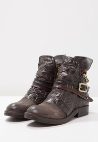 Bruine leren enkellaarsjes met een geometrisch reliëfpatroon, een zijrits en een bruine riem met een gouden gesp rond de enkel.