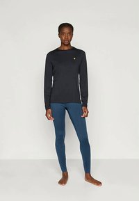 Fekete, hosszú ujjú póló kis emblémával és kék leggingszel. Az anyag simának tűnik, szorosan illeszkedik a testhez.