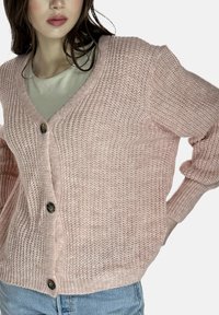 Różowy dziergany kardigan z dekoltem w serek, o luźnym kroju, z prążkowanymi mankietami i dwoma ciemnymi guzikami z przodu. Teksturowana tkanina o miękkim wyglądzie.