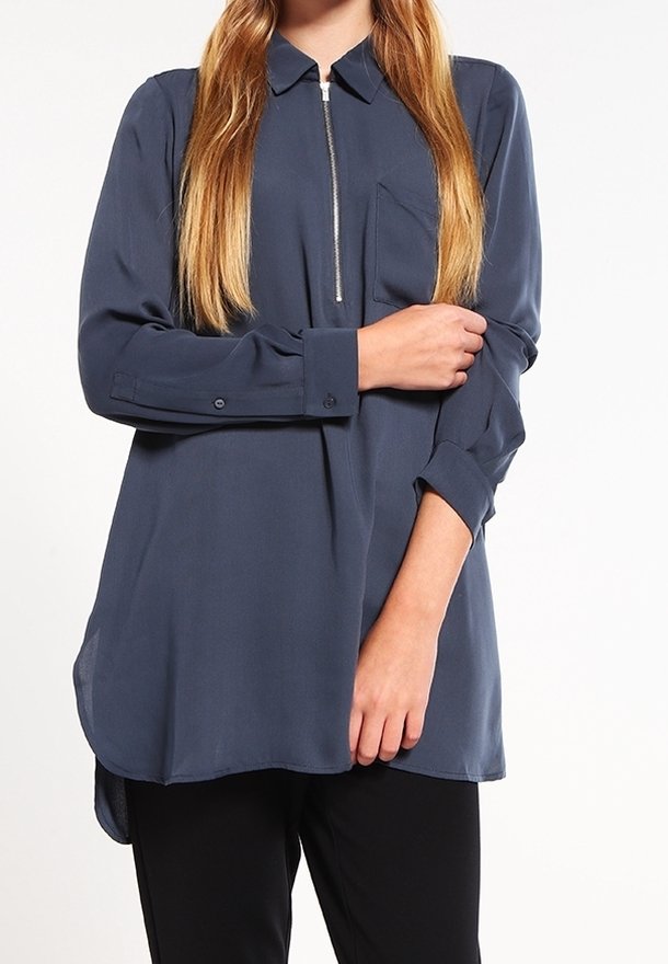 Blouse bleu marine à manches longues avec un détail de zip, un col, une poche poitrine unique et un ourlet incurvé. Tissu lisse et coupe décontractée.