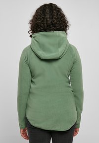 Felpa verde in pile con un design aderente, grande cappuccio e maniche lunghe. Tessuto liscio e orlo curvo sul retro.