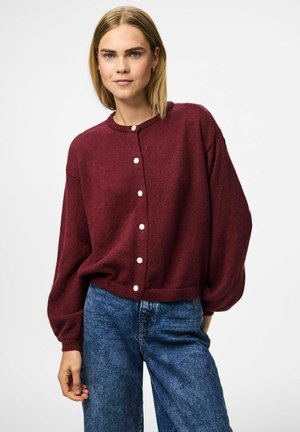 Burgundy cardigan made from textured knit fabric, featuring a round neck, front buttons, and loose-fit sleeves, paired with blue jeans.