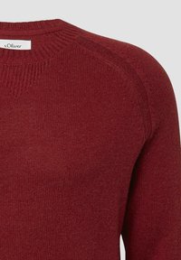 Bordowy sweter z dzianiny typu crewneck z prążkowanym kołnierzem i szwami na ramionach, z metką marki s.Oliver przy dekolcie.