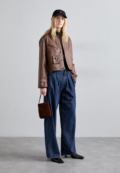 Brun læder cropped jakke med lommer, sort top, brede blå jeans og en lille brun quiltet håndtaske. Sort kasket og blanke sorte sko.