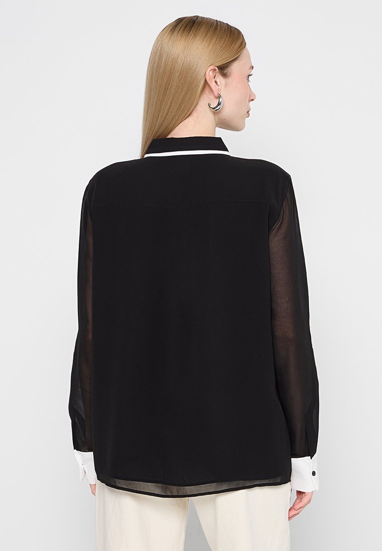 Schwarze, durchsichtige Bluse mit einem kontrastierenden weißen Kragen und Manschetten, geradem Schnitt und feinen Faltendetails am Rücken.