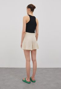 Zwarte mouwloze top, beige uitlopende shorts en groene instapsandalen. Gladde stof; eenvoudig ontwerp; neutrale kleuren; geen zichtbare patronen of hardware.
