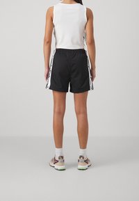 Black athletic shorts with white side stripes and snap buttons, paired with a white cropped tank top and beige sneakers. Smooth texture.