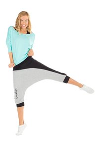 Top largo de manga larga en teal claro oversized combinado con pantalones harem negros y grises con tobillos ajustados. Zapatillas blancas completan el look.