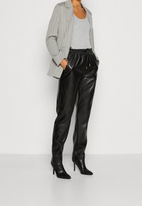 Grijs gestreepte blazer, grijze tanktop en zwarte leren broek met een elastische tailleband. Zwarte hoge laarzen maken de outfit compleet.