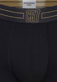 Czarne bawełniane bokserki z złotym paskiem w talii. Z logo 'CR7' i poziomymi paskami. Metka wskazuje rozmiar "Medium". Gładka faktura.