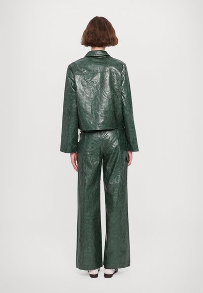 Giacca in finta pelle verde, arricciata e con un design cropped, abbinata a pantaloni larghi. Presenta un colletto a risvolto e una vestibilità comoda.