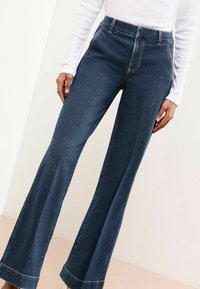 Donkerblauwe spijkerbroek met een flared pasvorm en hoge taille, met een soepele textuur, zichtbare stiksels en een wijde pijpopening aan de onderkant.