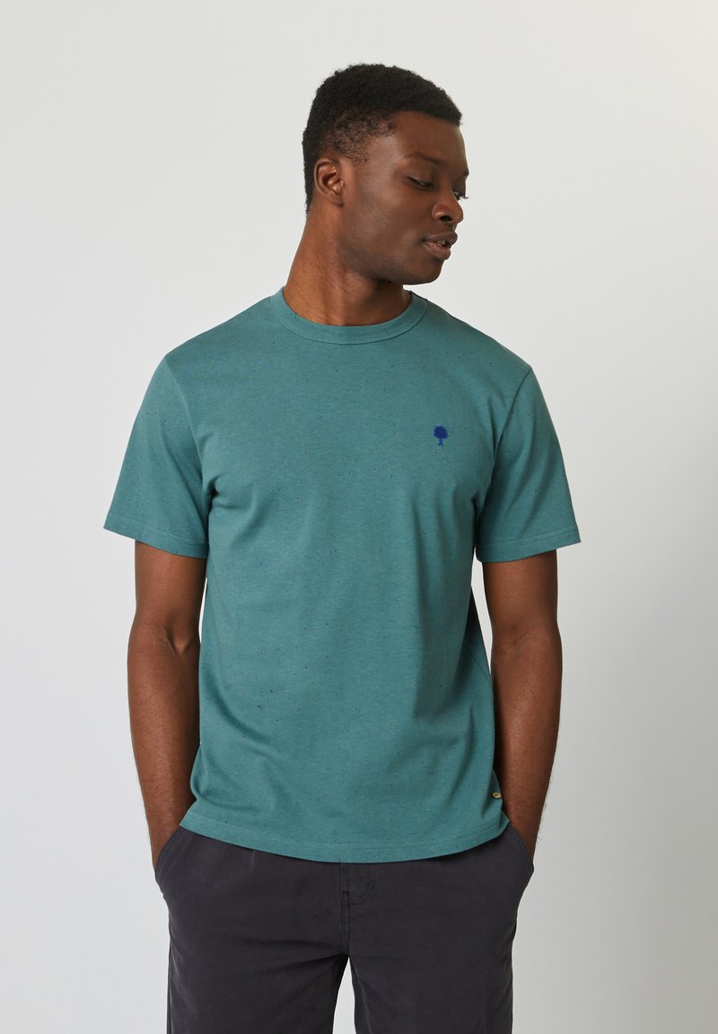 Teal katoenen t-shirt met een subtiele gespikkelde textuur, ronde halslijn, korte mouwen en een klein donkerblauw boomlogo op de borst.