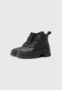 Botas de cuero negras hasta el tobillo con un acabado texturizado, que cuentan con una cremallera lateral, un frente con cordones y una suela gruesa con un patrón de relieve rectangular.