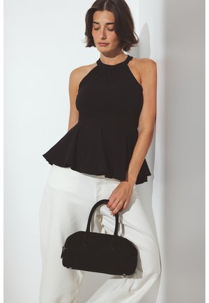 Sort halterneck peplum-top med tætsiddende liv og udvidet kant, parret med højtaljede hvide bukser og en lille sort håndtaske.