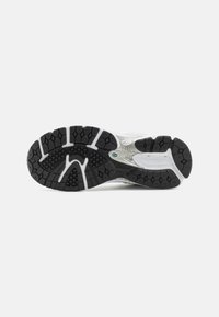 Semelle d'une chaussure de course blanche et noire avec un motif texturé et un logo de marque visible sous la voûte, sur un fond blanc uni.