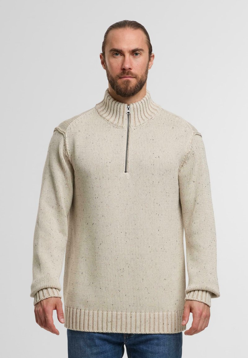 Strikket sweater i beige med høj krave, halv lynlås foran og ribbede manchetter. Har et tekstureret mønster med indslag af mørkere farver.