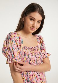 Rochie cu imprimeu floral în roz, cu mâneci bufante, decolteu pătrat și bust smockat, având un detaliu cu panglică în față. Textură de țesătură moale.