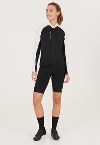 Schwarze Radjacke mit weißen Ärmeln, Reißverschluss vorne und schwarzen Shorts. Bietet eine enge Passform, weichen Stoff und minimalen Branding auf der Jacke.